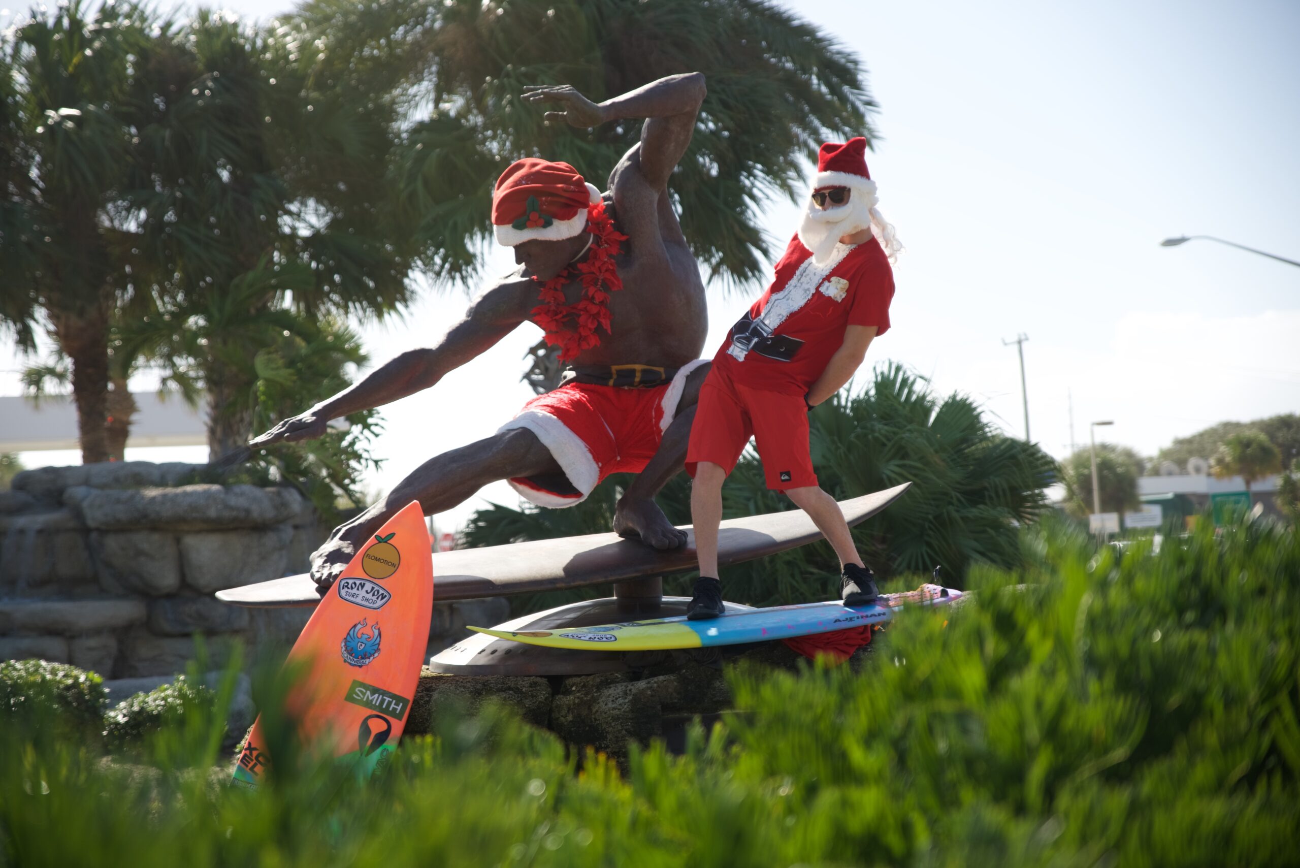 A Surfing Santa poses at the Kelly Slater statue (also wearing Santa Costume) in Cocoa Beach